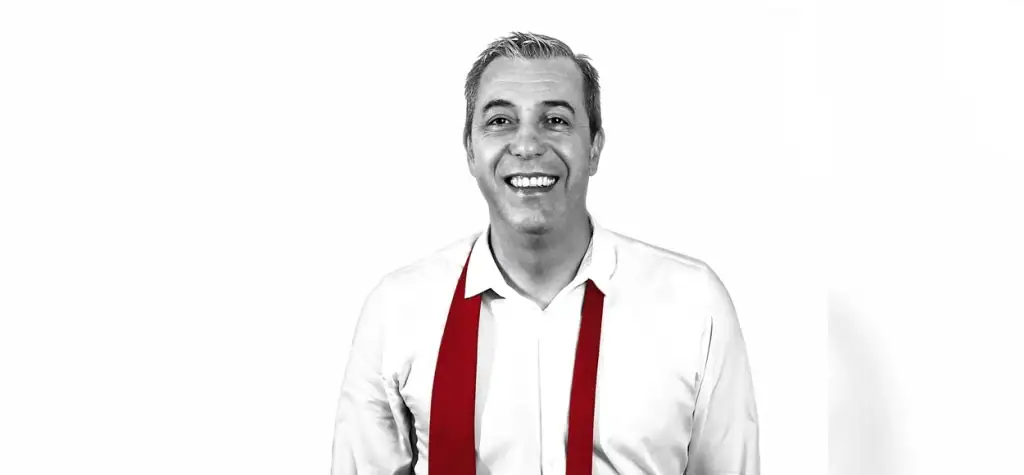 Hombre sonriendo con corbata roja y camisa blanca.