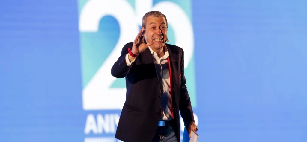 Hombre en conferencia con fondo de logo y texto.