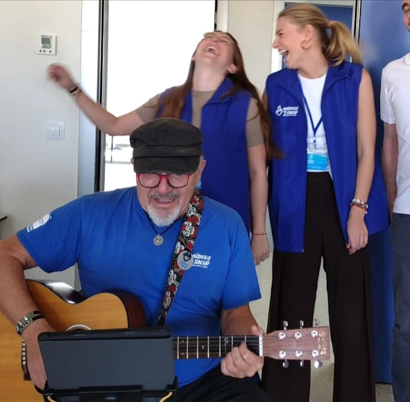Hombre tocando guitarra y riendo con mujeres en evento solidario.